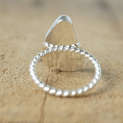 back view of A sterling silver ring featuring teardrop-shaped black sea glass, on a textured light brown wood surface.