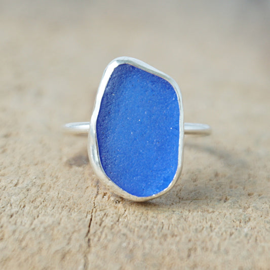 a silver ring with cobalt blue sea glass, on a wooden surface.