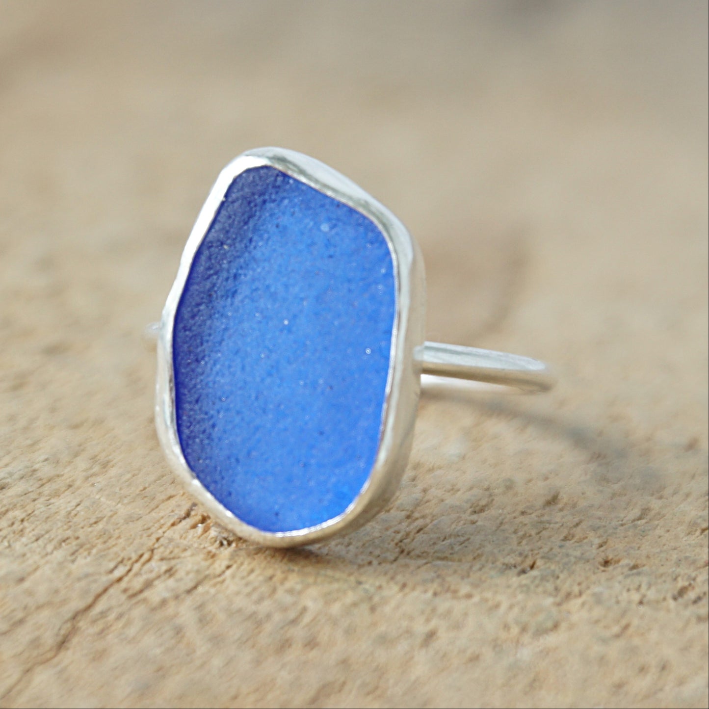 a silver ring with cobalt blue sea glass, on a wooden surface.