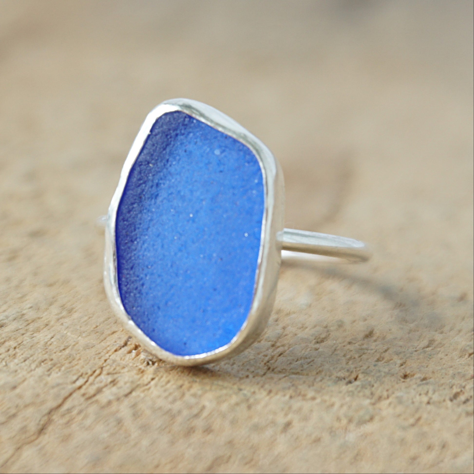 a silver ring with cobalt blue sea glass, on a wooden surface.