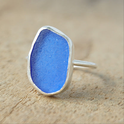 a silver ring with cobalt blue sea glass, on a wooden surface.