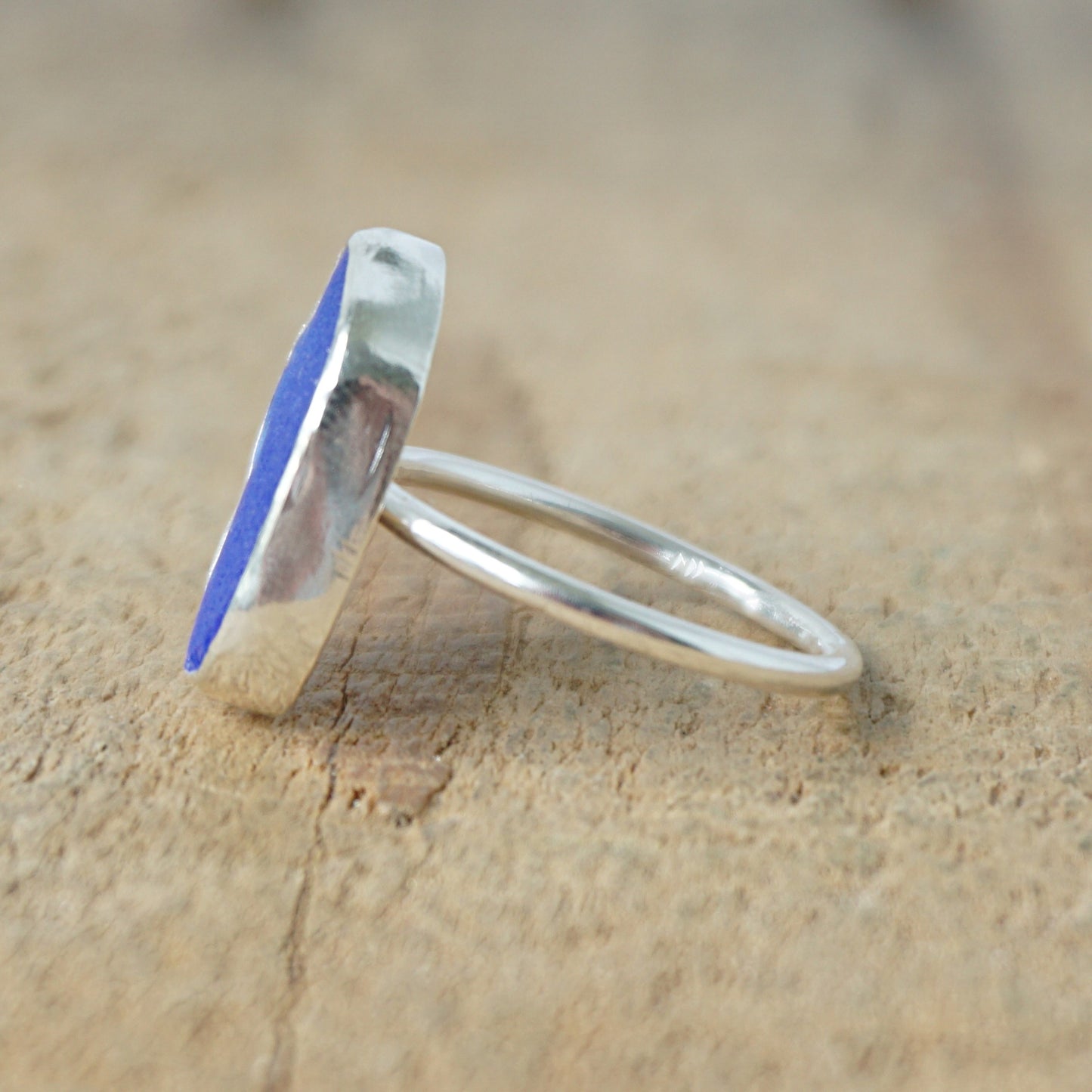 side view of a silver ring with cobalt blue sea glass, on a wooden surface.