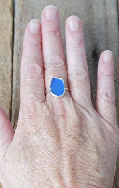 hand wearing a silver ring with cobalt blue sea glass, on a wooden surface.