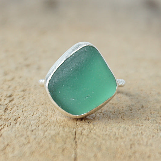 a silver ring with dark green sea glass, on a wooden surface.