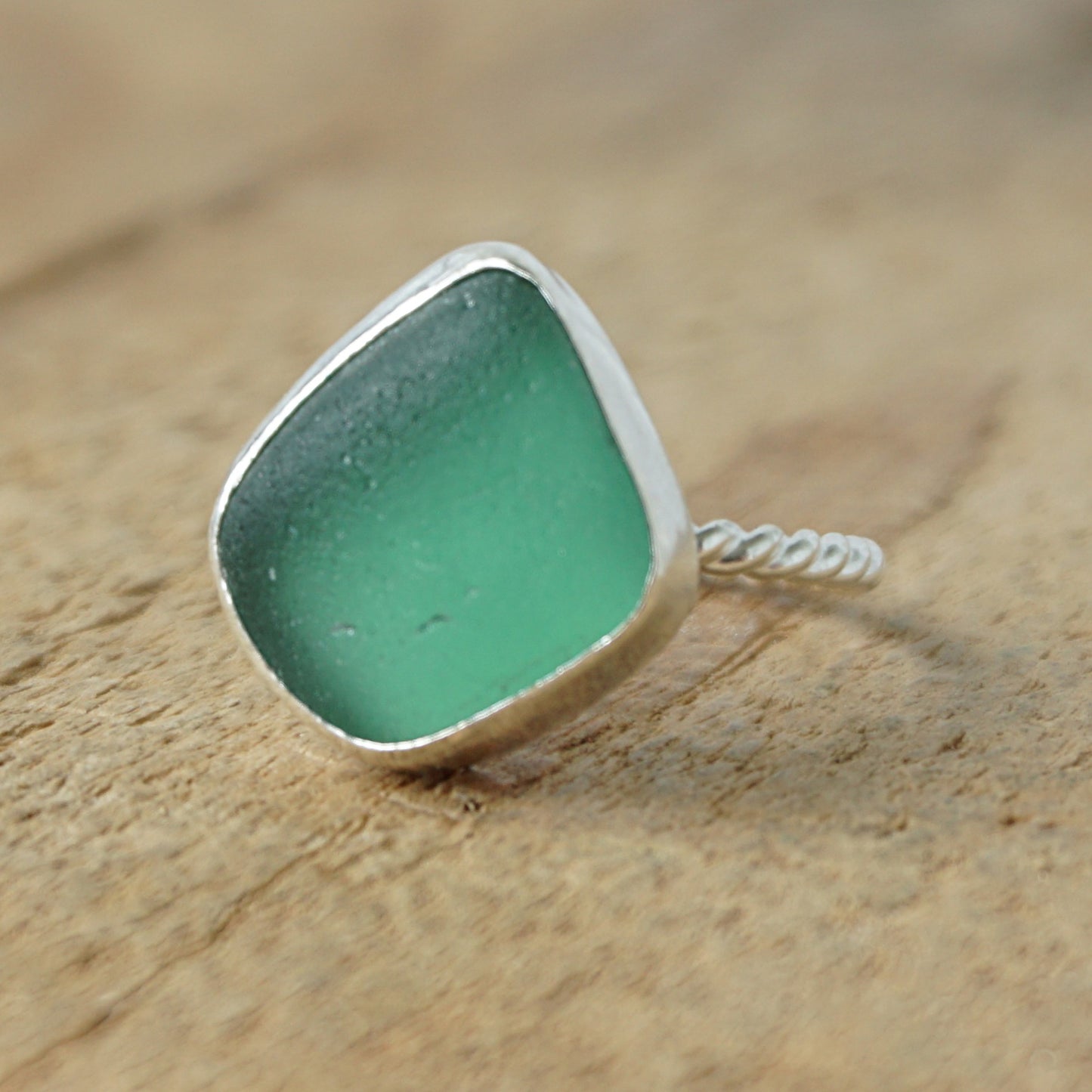 a silver ring with dark green sea glass, on a wooden surface.