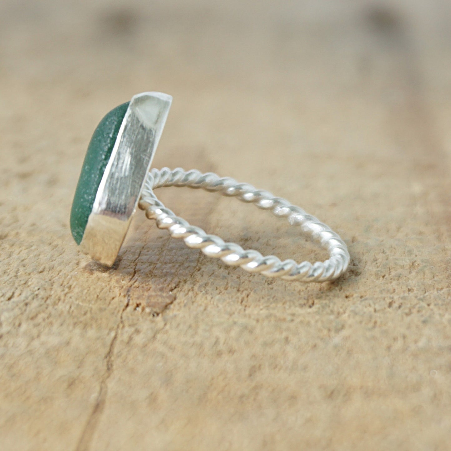 side view of a silver ring with dark green sea glass, on a wooden surface.