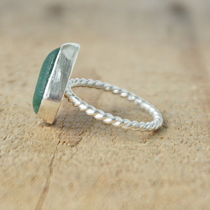 side view of a silver ring with dark green sea glass, on a wooden surface.