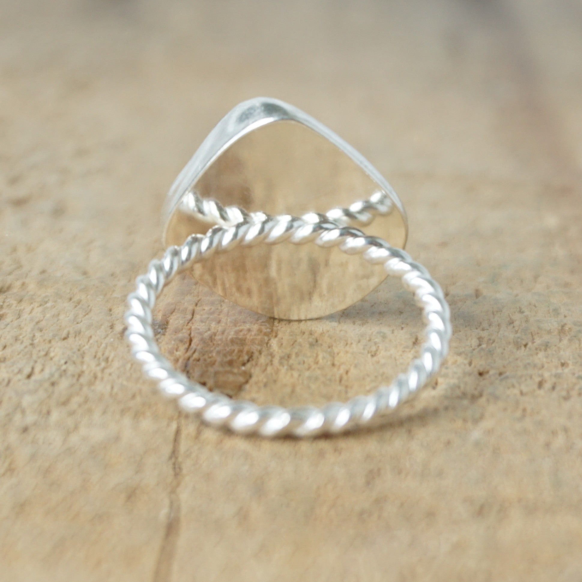 back view of a silver ring with dark green sea glass, on a wooden surface.