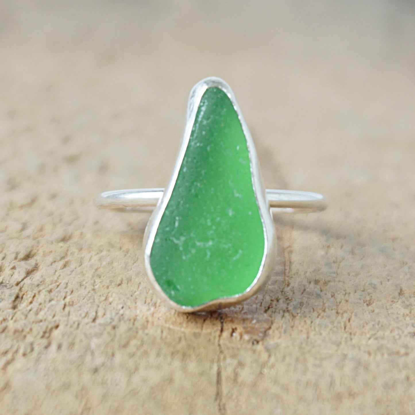 a silver ring with kelly green sea glass, on a wooden surface.