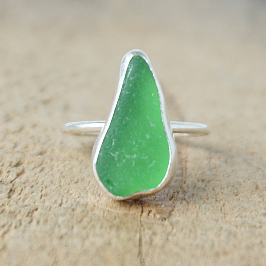 a silver ring with kelly green sea glass, on a wooden surface.