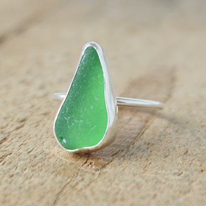 a silver ring with kelly green sea glass, on a wooden surface.