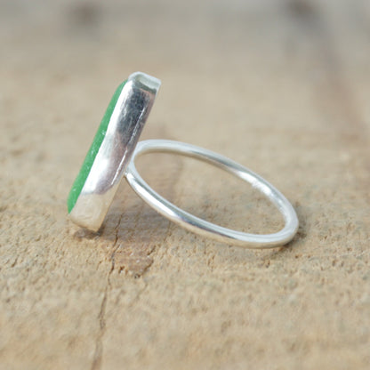side view of a silver ring with kelly green sea glass, on a wooden surface.