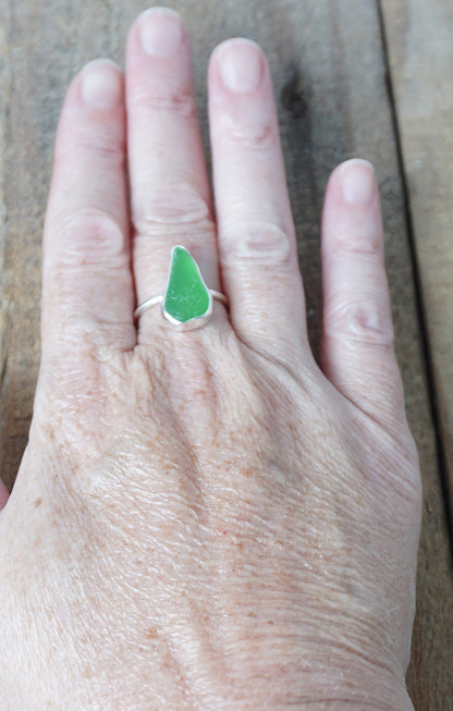 hand wearing a silver ring with kelly green sea glass, on a wooden surface.
