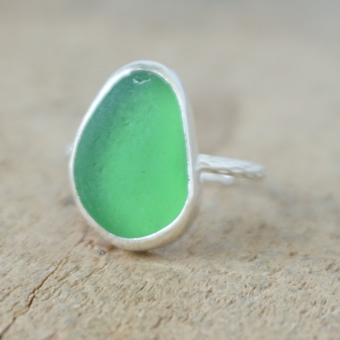 a silver ring with kelly green sea glass, on a wooden surface.