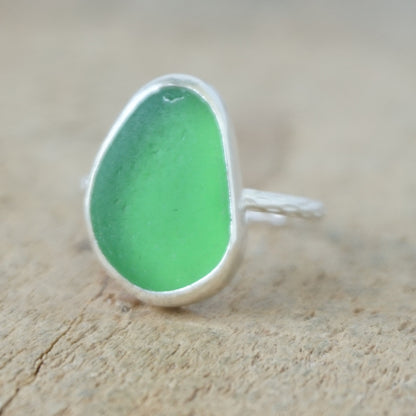a silver ring with kelly green sea glass, on a wooden surface.
