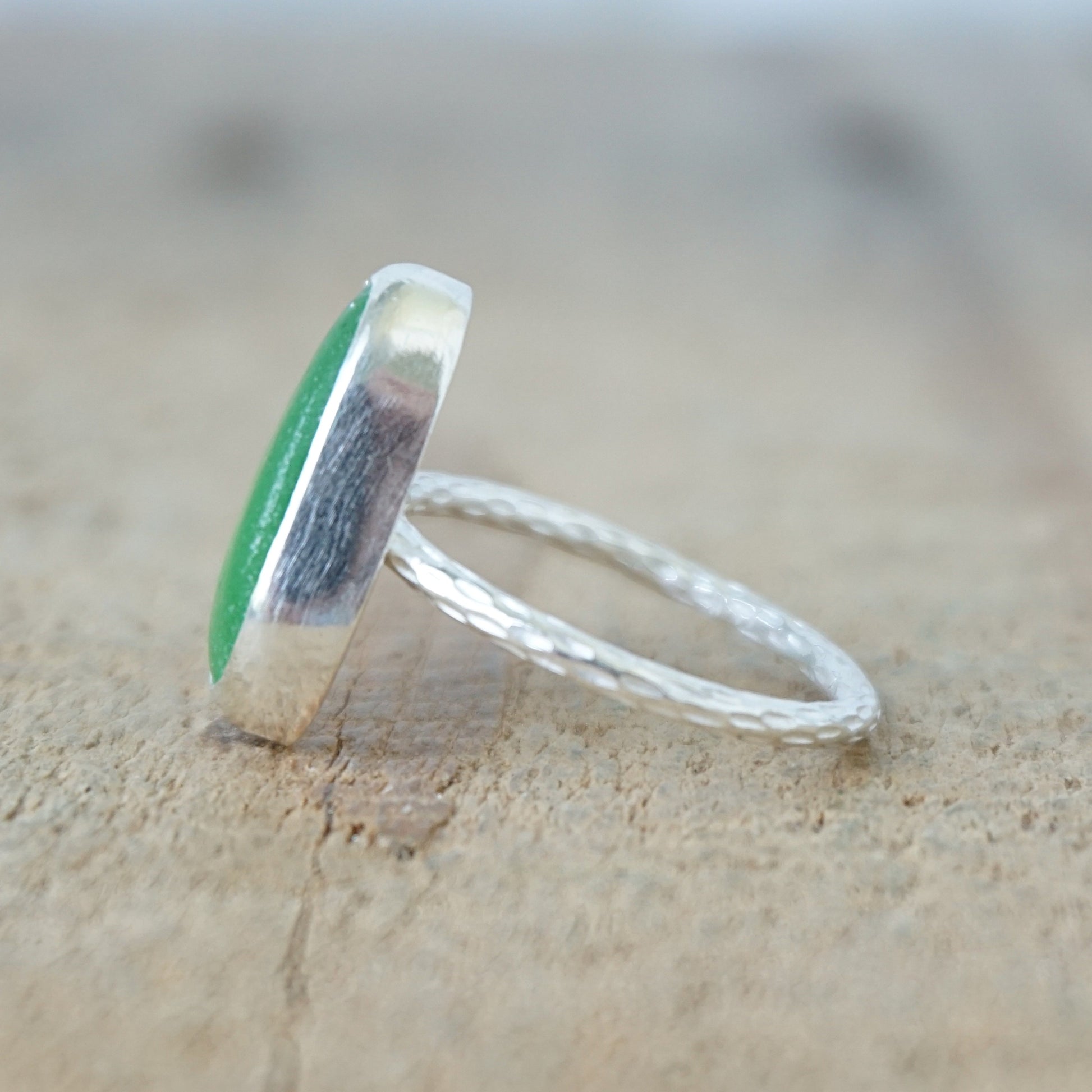 side view of a silver ring with kelly green sea glass, on a wooden surface.