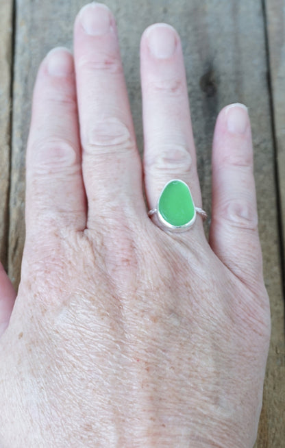 hand wearing a silver ring with kelly green sea glass, on a wooden surface.