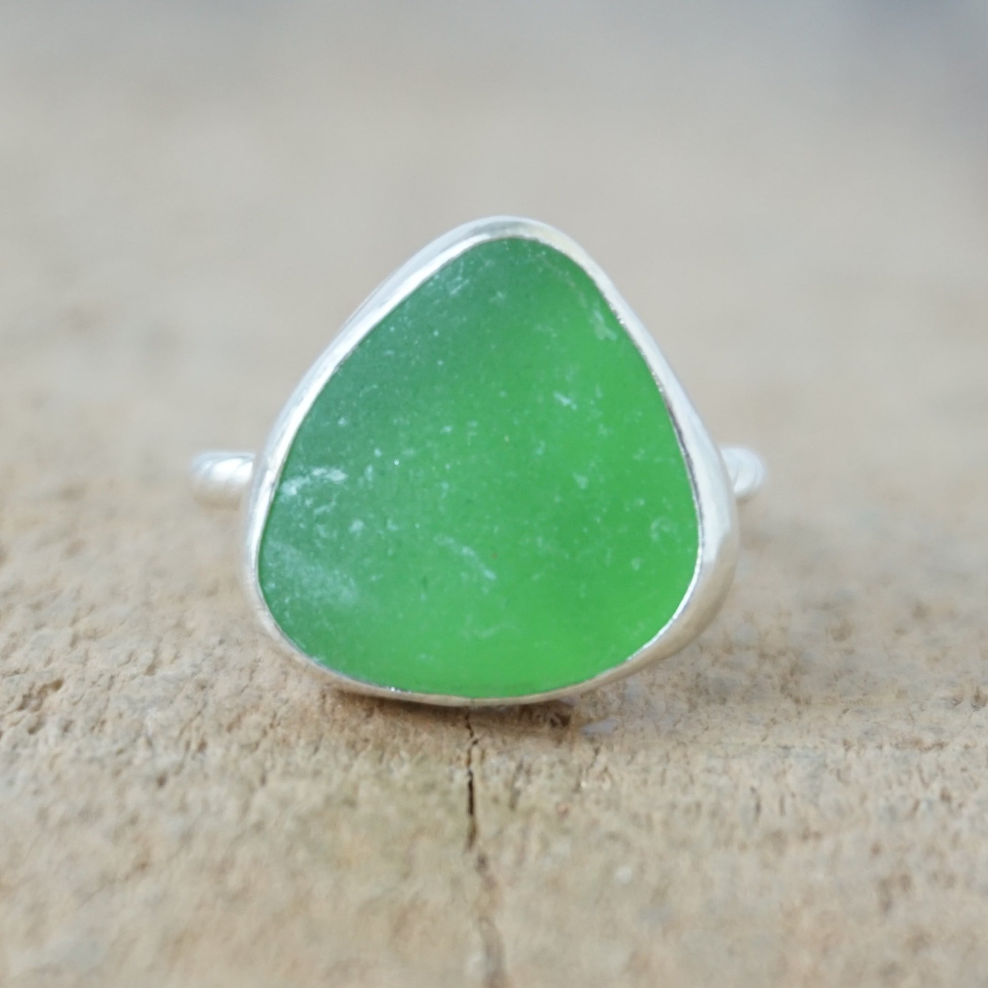 a silver ring with kelly green sea glass, on a wooden surface.