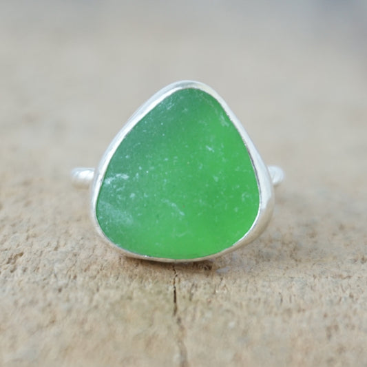 a silver ring with kelly green sea glass, on a wooden surface.