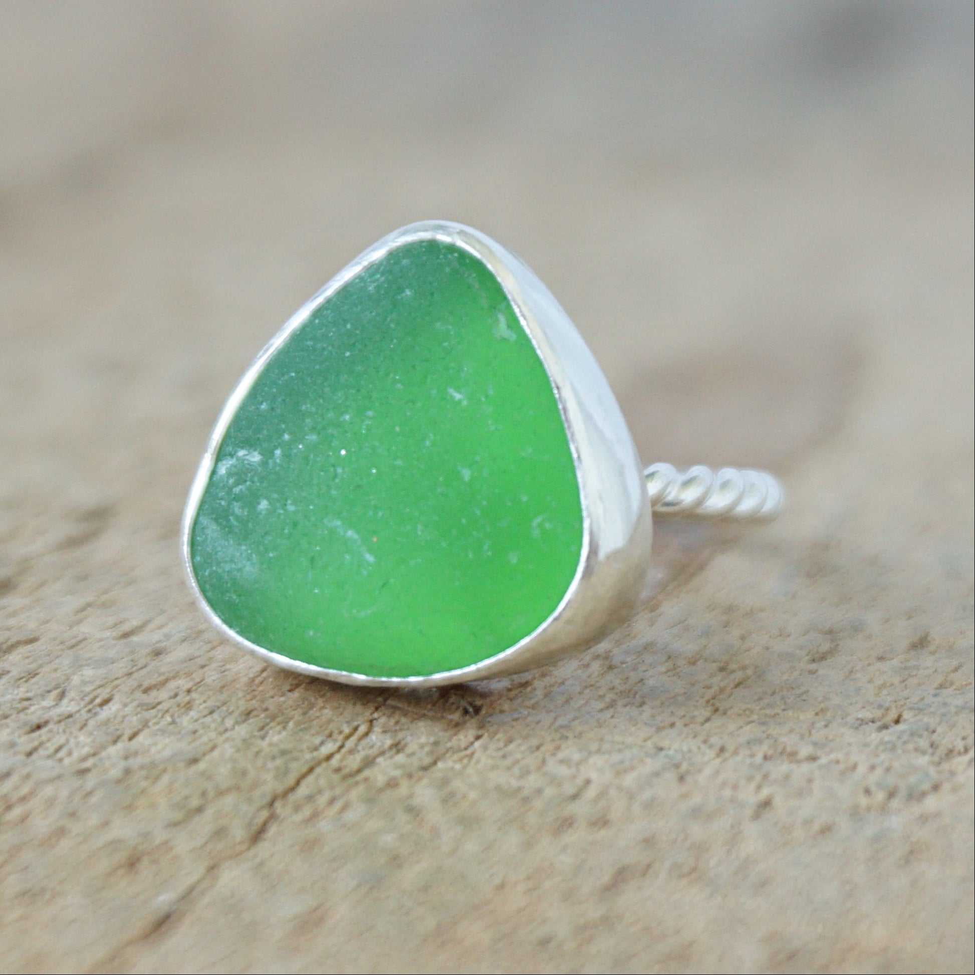 a silver ring with kelly green sea glass, on a wooden surface.