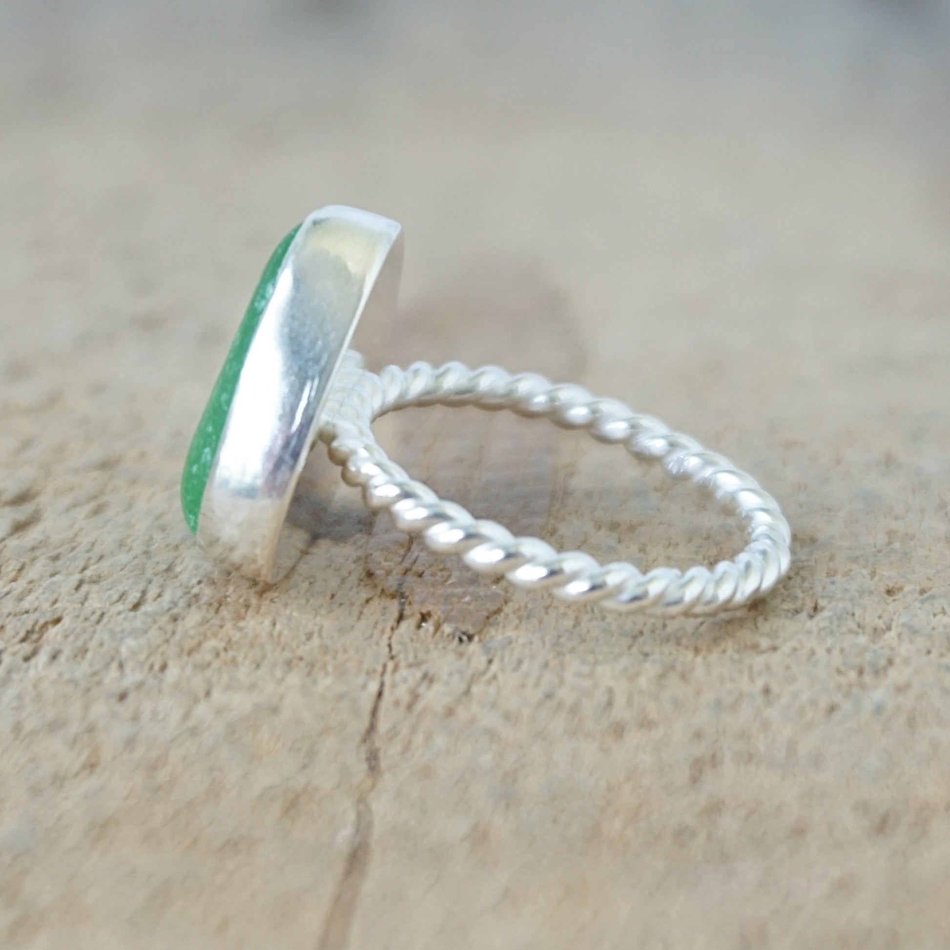 side view of a silver ring with kelly green sea glass, on a wooden surface.