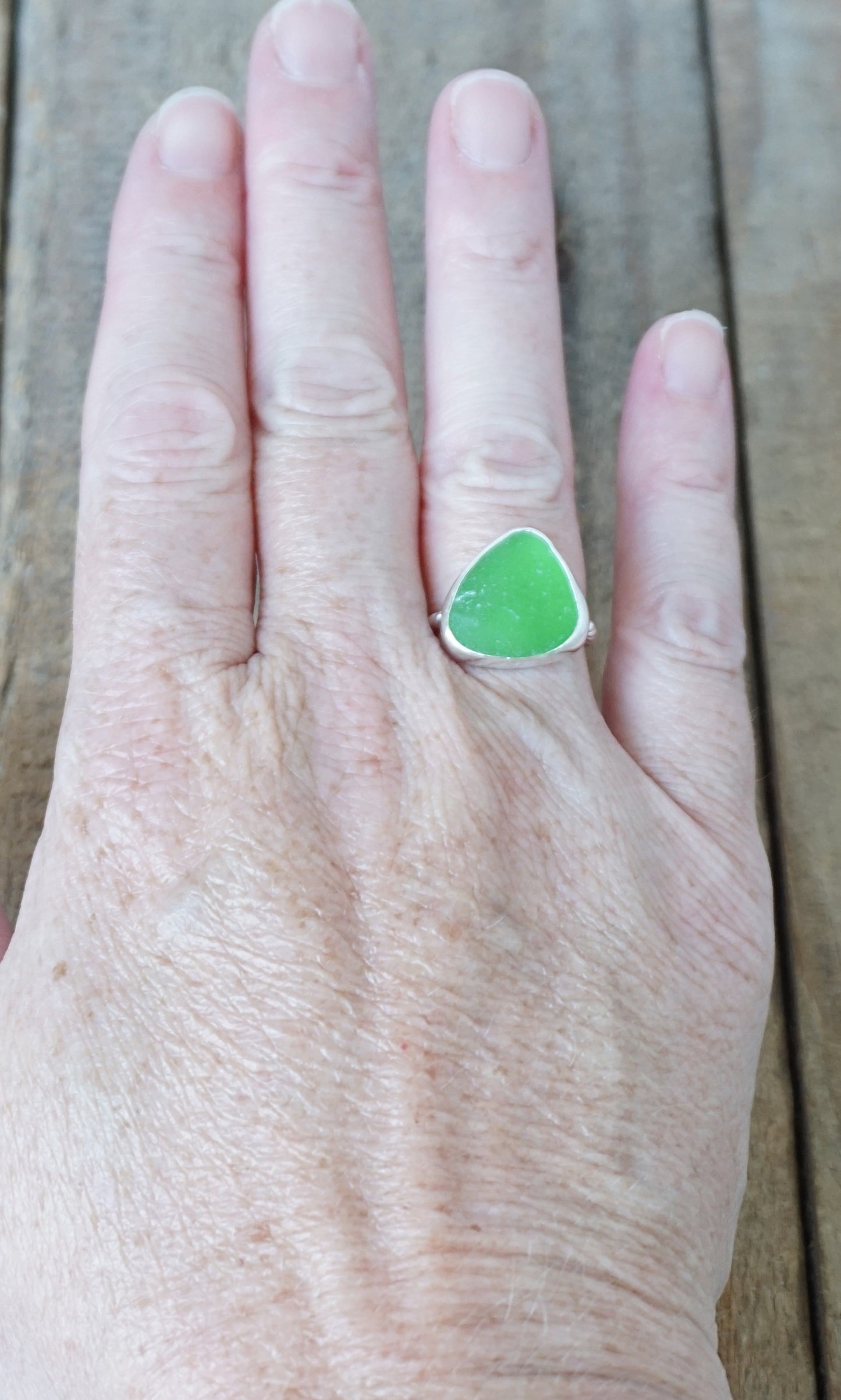 hand wearing a silver ring with kelly green sea glass, on a wooden surface.