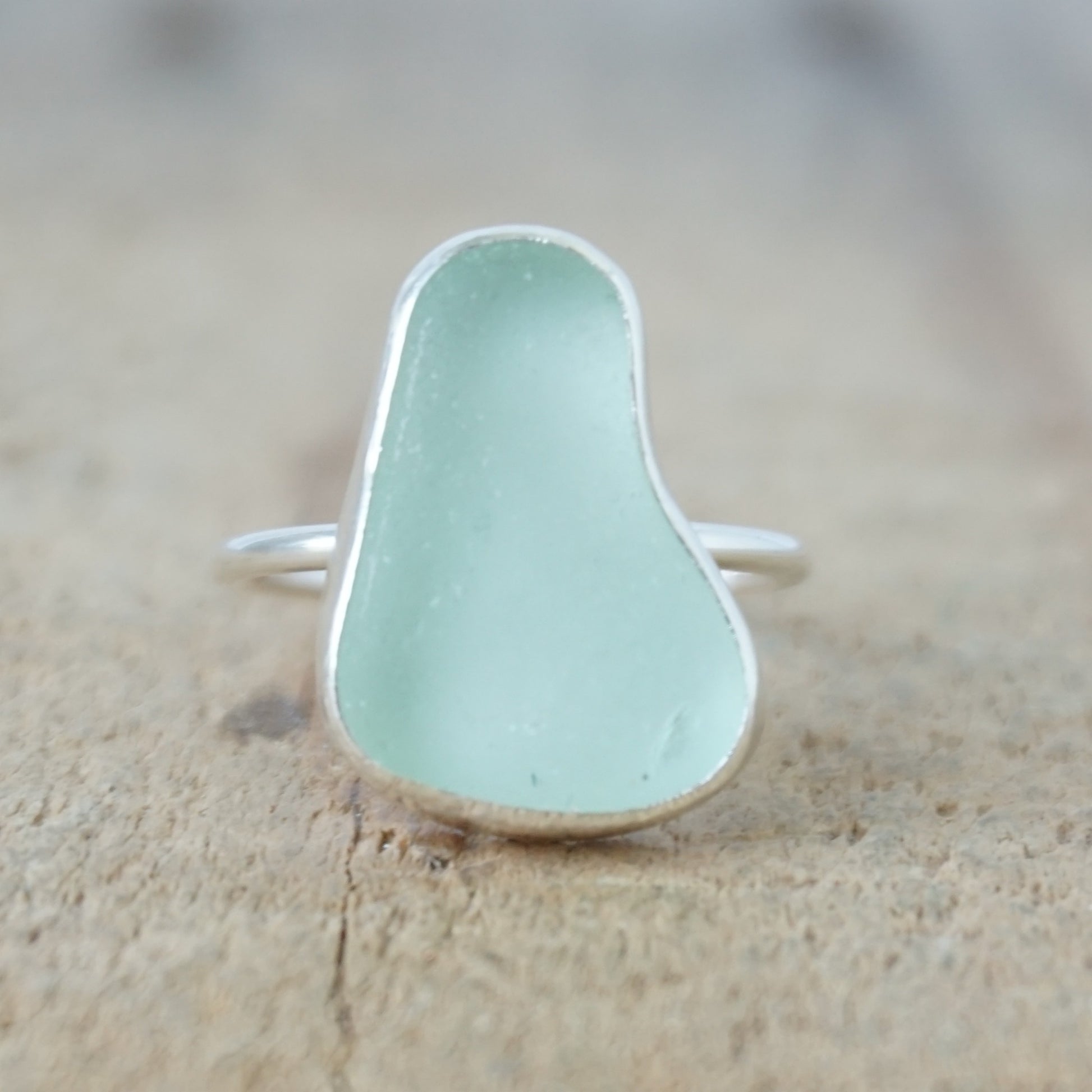 a silver ring with seafoam green sea glass, on a wooden surface.