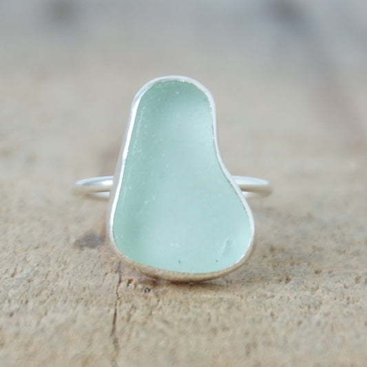 a silver ring with seafoam green sea glass, on a wooden surface.