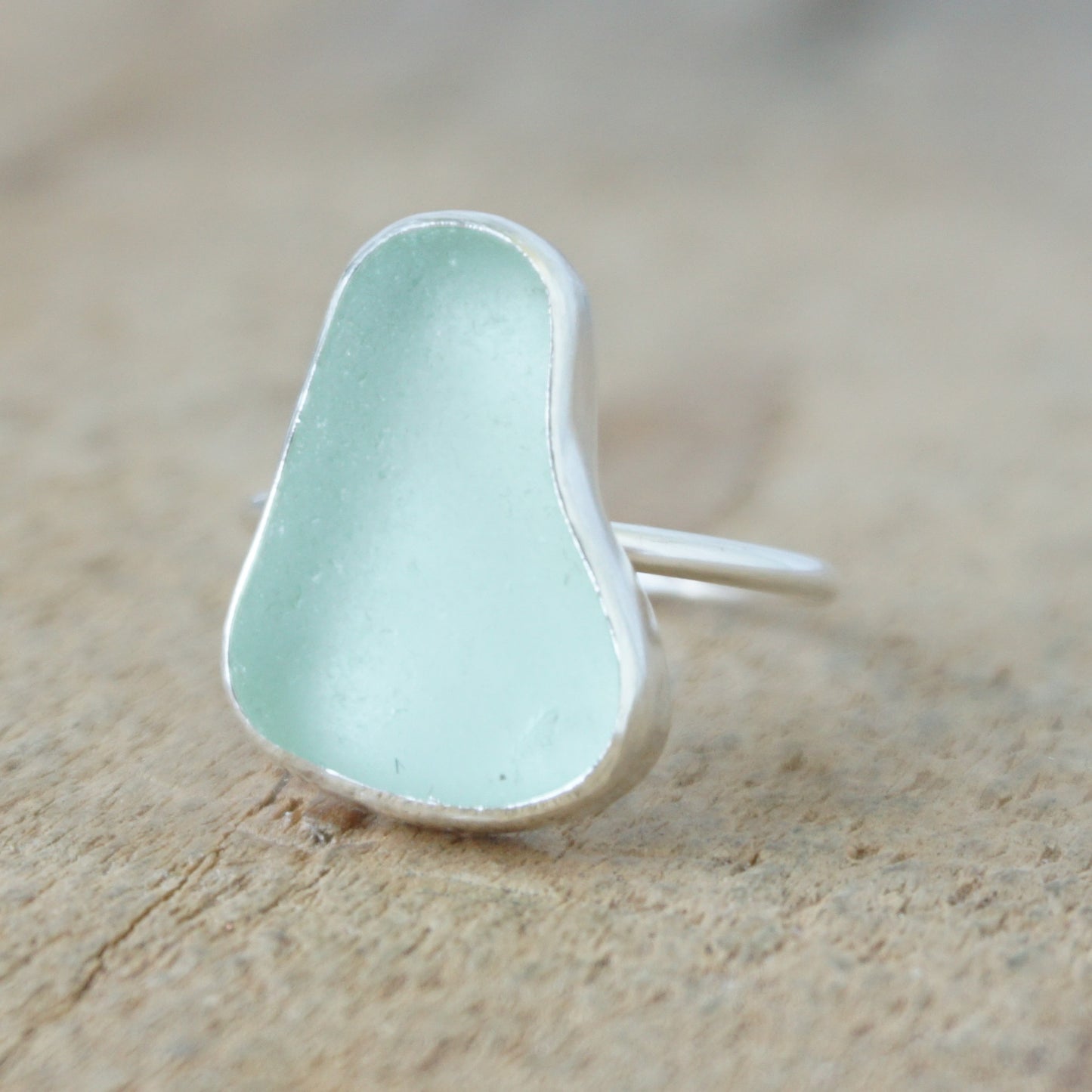 a silver ring with seafoam green sea glass, on a wooden surface.
