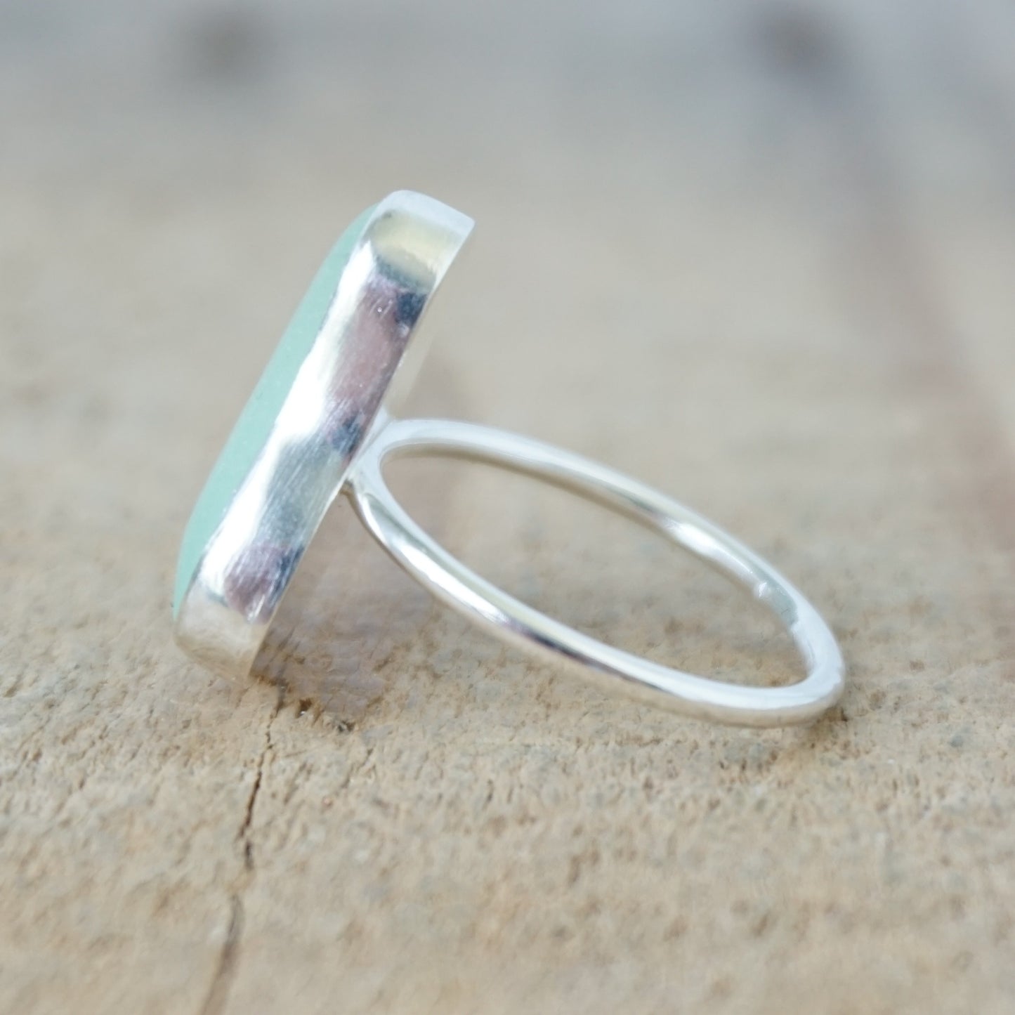 side view of a silver ring with seafoam green sea glass, on a wooden surface.
