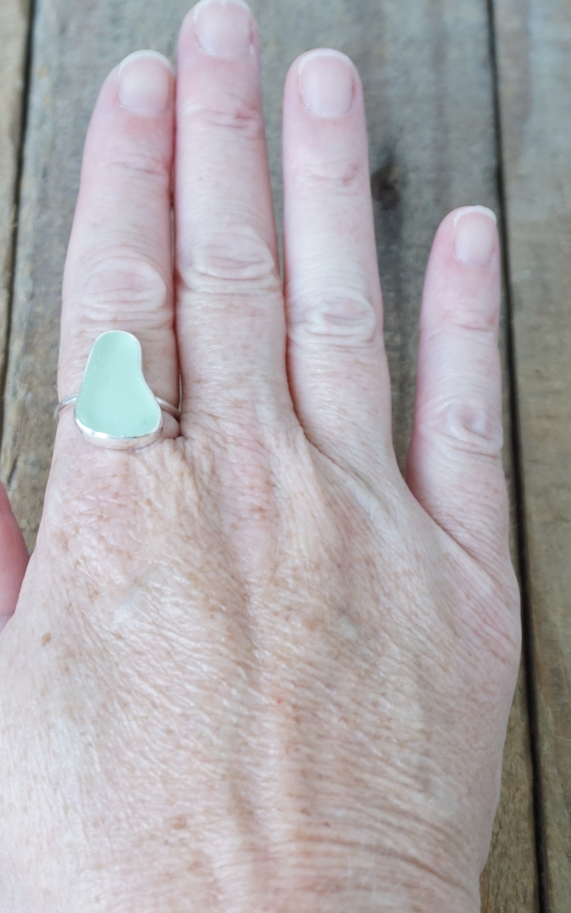 hand wearing a silver ring with seafoam green sea glass, on a wooden surface.