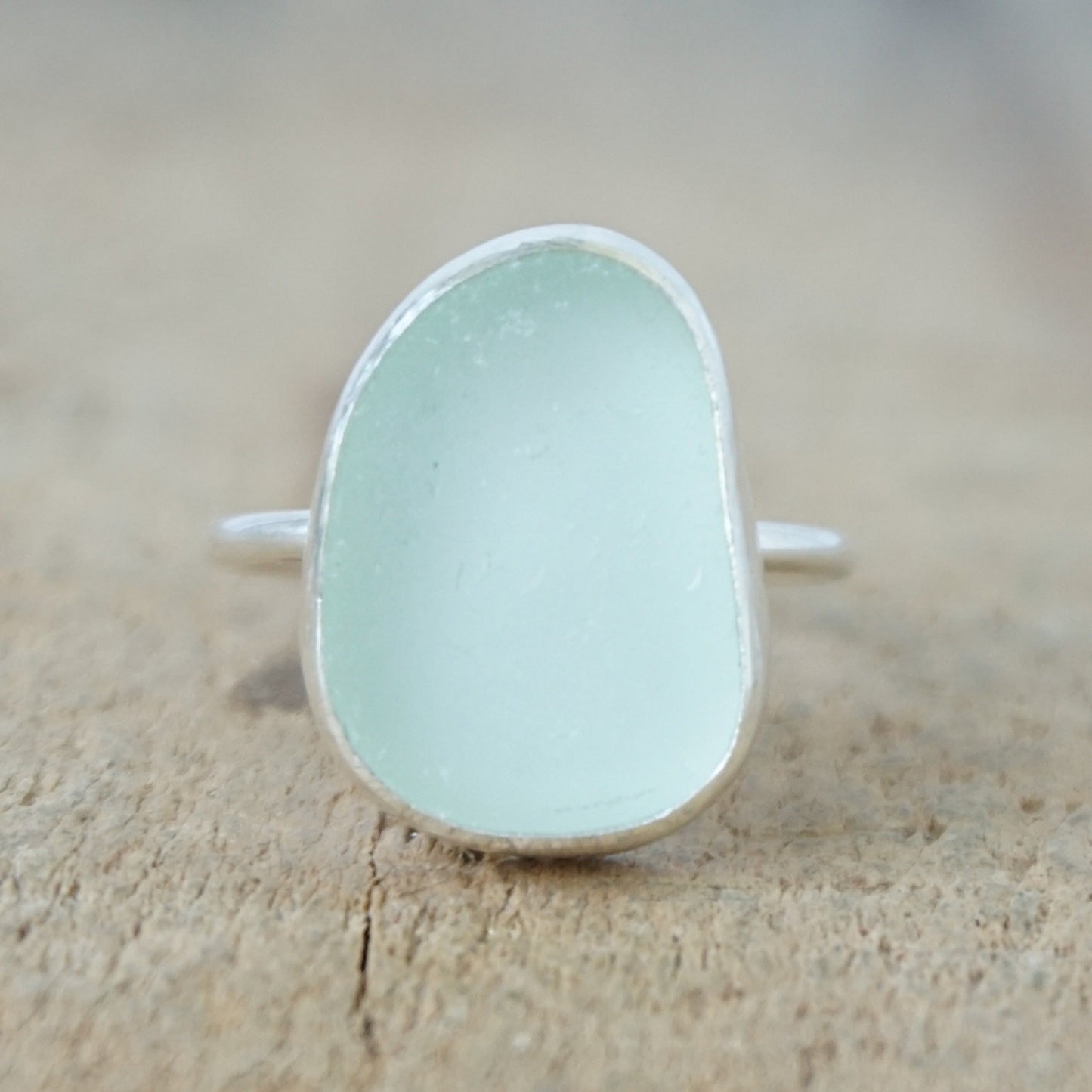 a silver ring with seafoam green sea glass, on a wooden surface.
