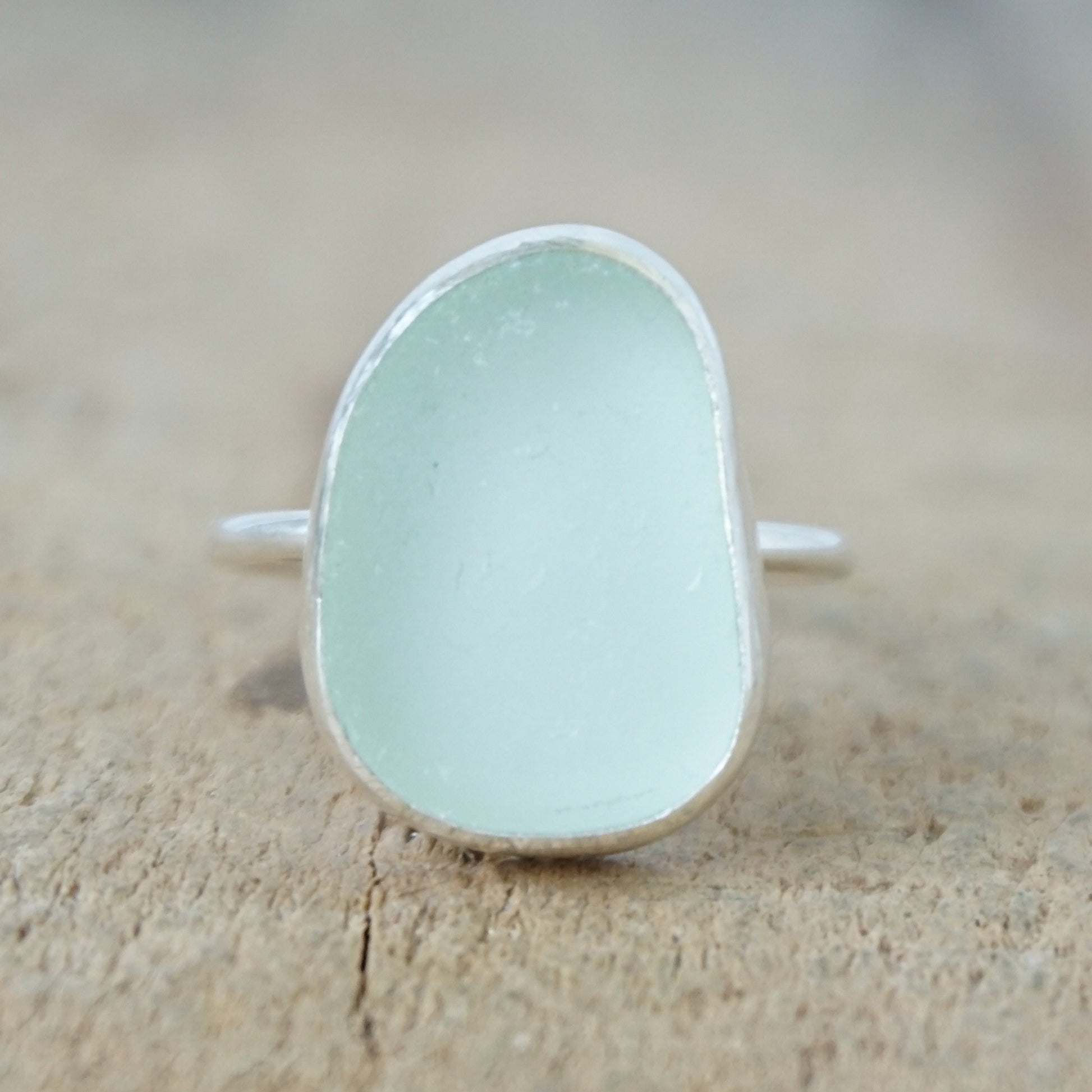 a silver ring with seafoam green sea glass, on a wooden surface.