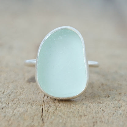 a silver ring with seafoam green sea glass, on a wooden surface.