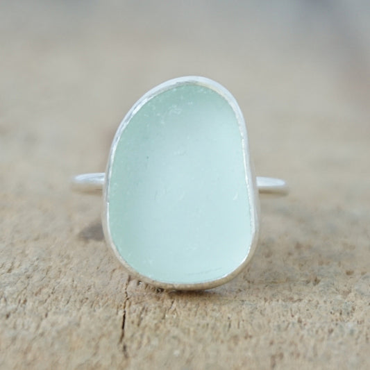 a silver ring with seafoam green sea glass, on a wooden surface.