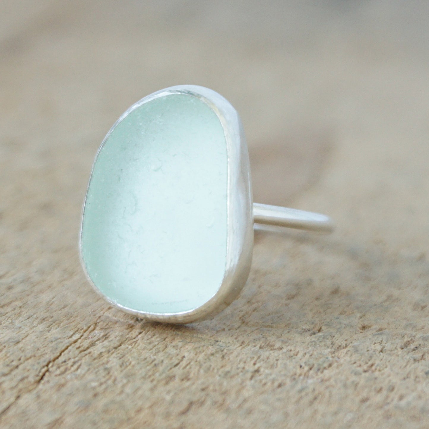 a silver ring with seafoam green sea glass, on a wooden surface.