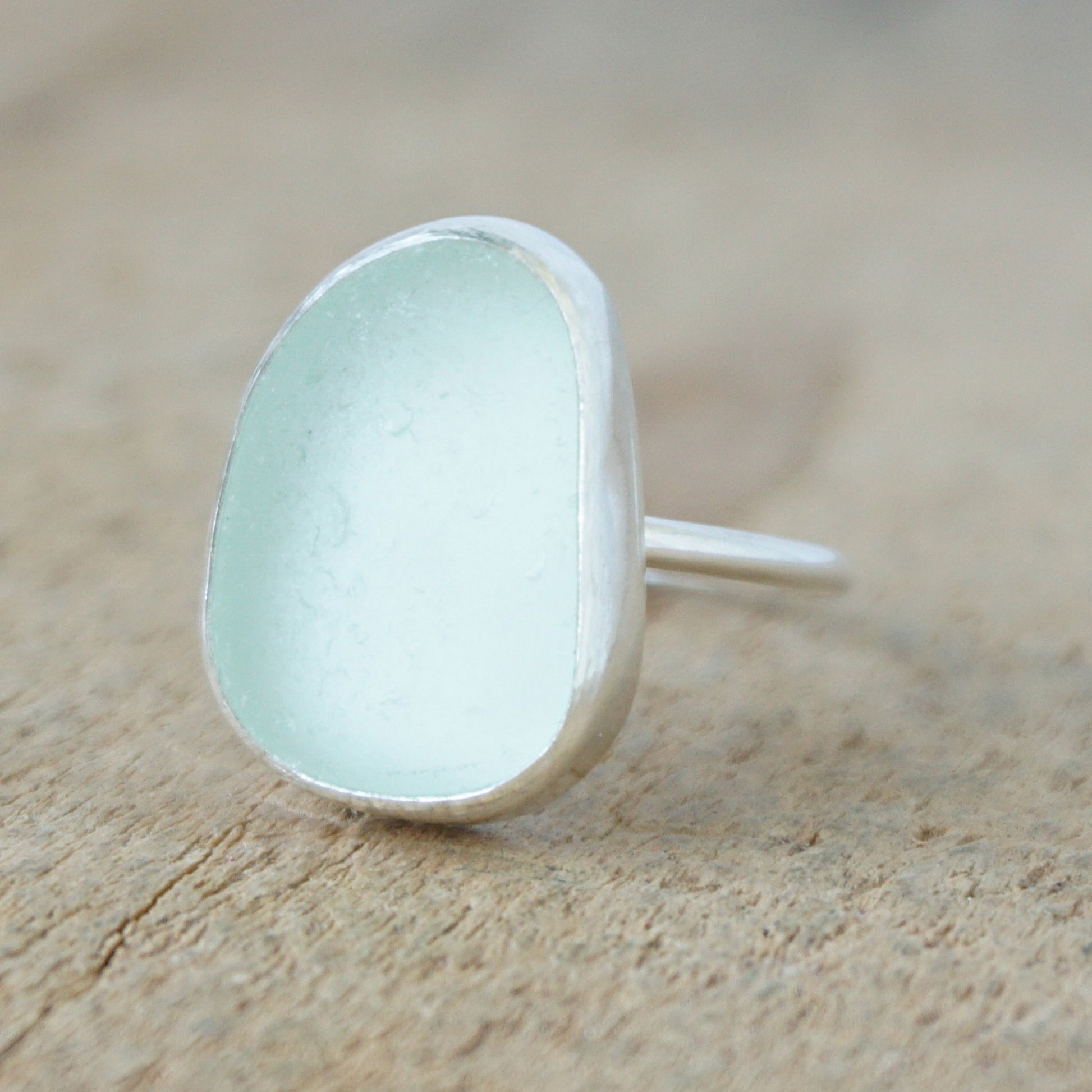 a silver ring with seafoam green sea glass, on a wooden surface.