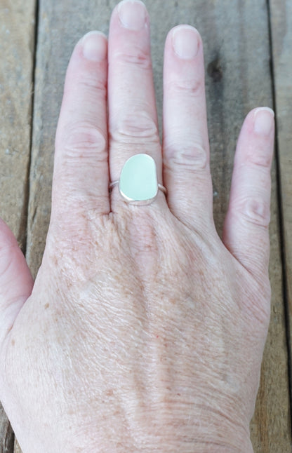 hand wearing a silver ring with seafoam green sea glass, on a wooden surface.