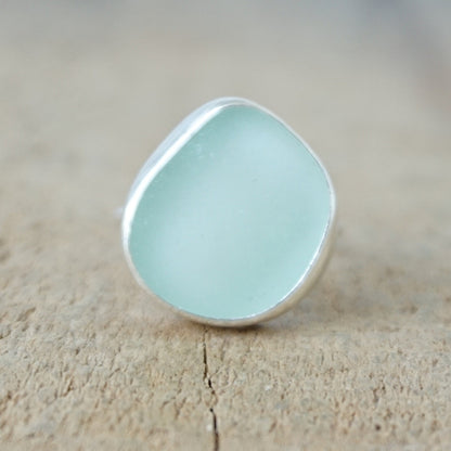 a silver ring with seafoam green sea glass, on a wooden surface.