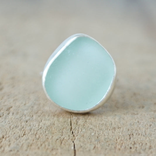 a silver ring with seafoam green sea glass, on a wooden surface.