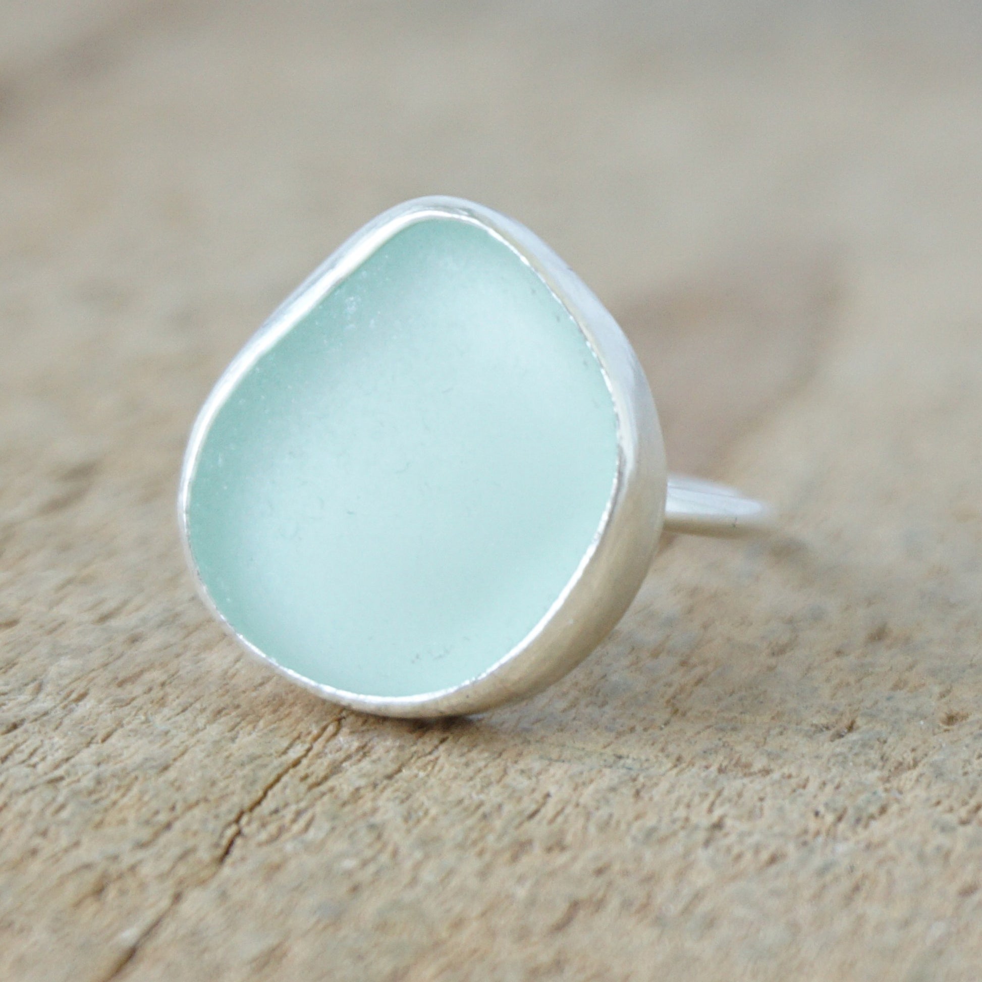 a silver ring with seafoam green sea glass, on a wooden surface.