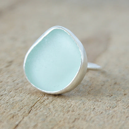 a silver ring with seafoam green sea glass, on a wooden surface.