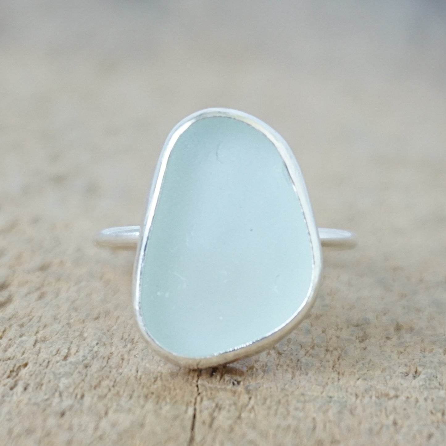 a silver ring with seafoam green sea glass, on a wooden surface.