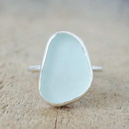 a silver ring with seafoam green sea glass, on a wooden surface.