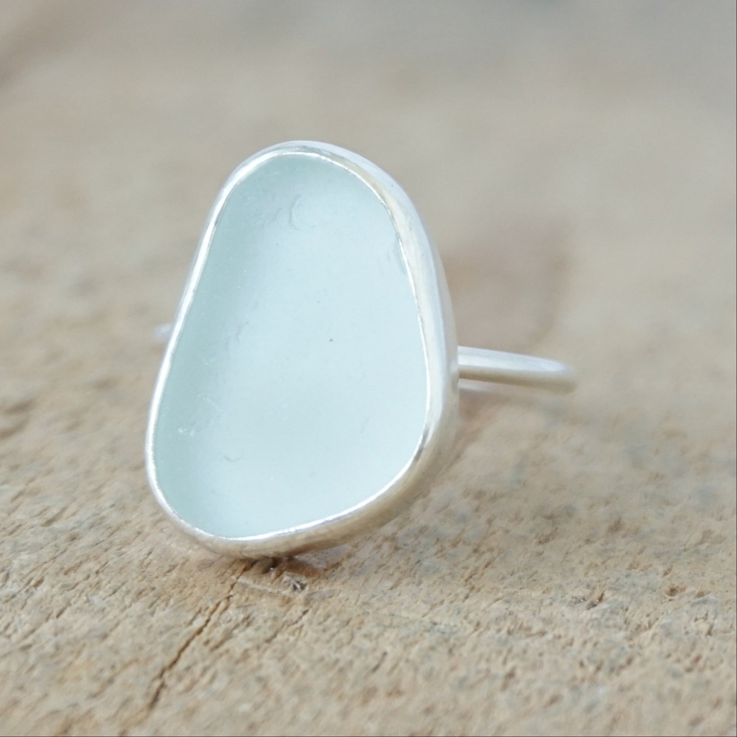a silver ring with seafoam green sea glass, on a wooden surface.