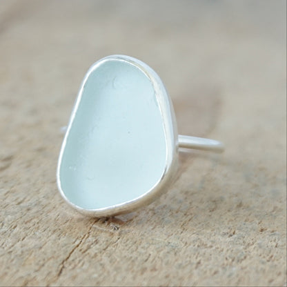 a silver ring with seafoam green sea glass, on a wooden surface.