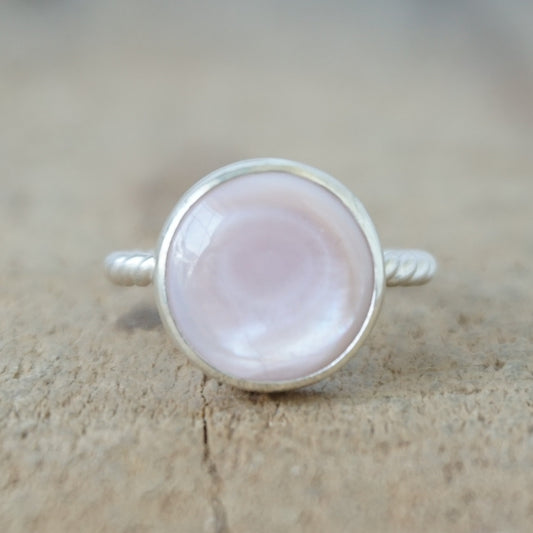 A silver ring featuring a round, smooth pale pink stone, on a wooden surface.