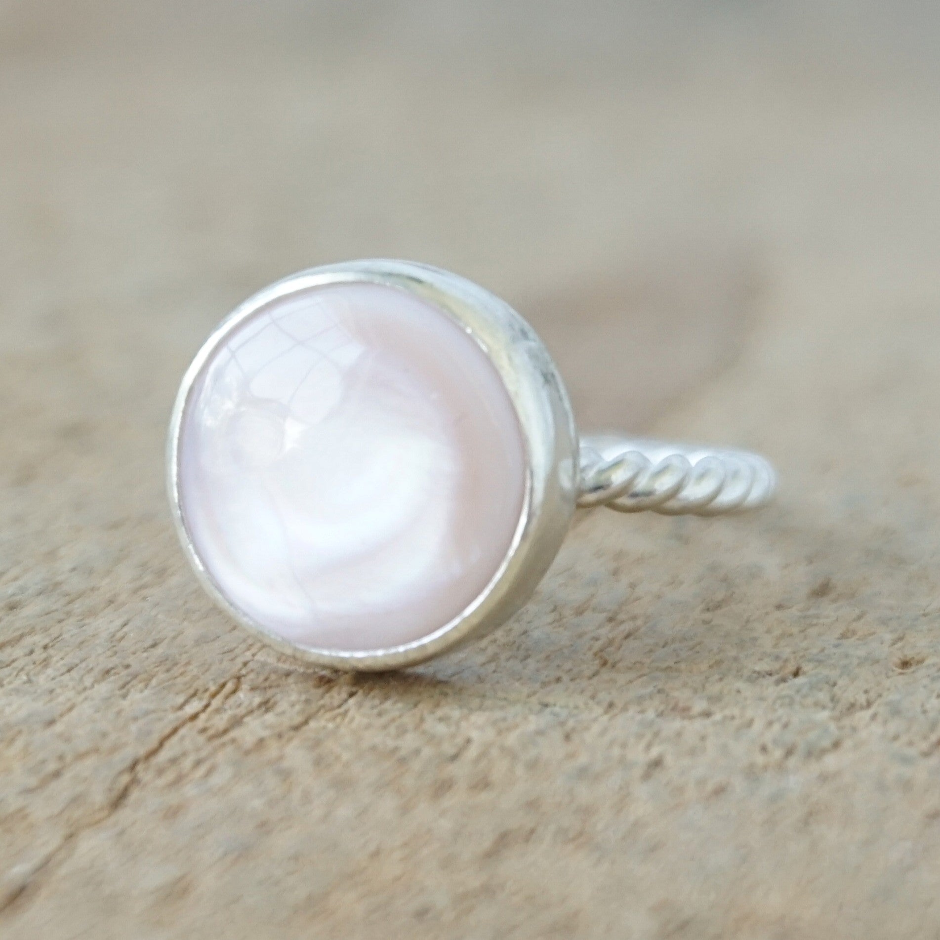 A silver ring featuring a round, smooth pale pink stone, on a wooden surface.