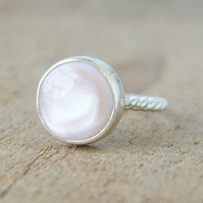 A silver ring featuring a round, smooth pale pink stone, on a wooden surface.