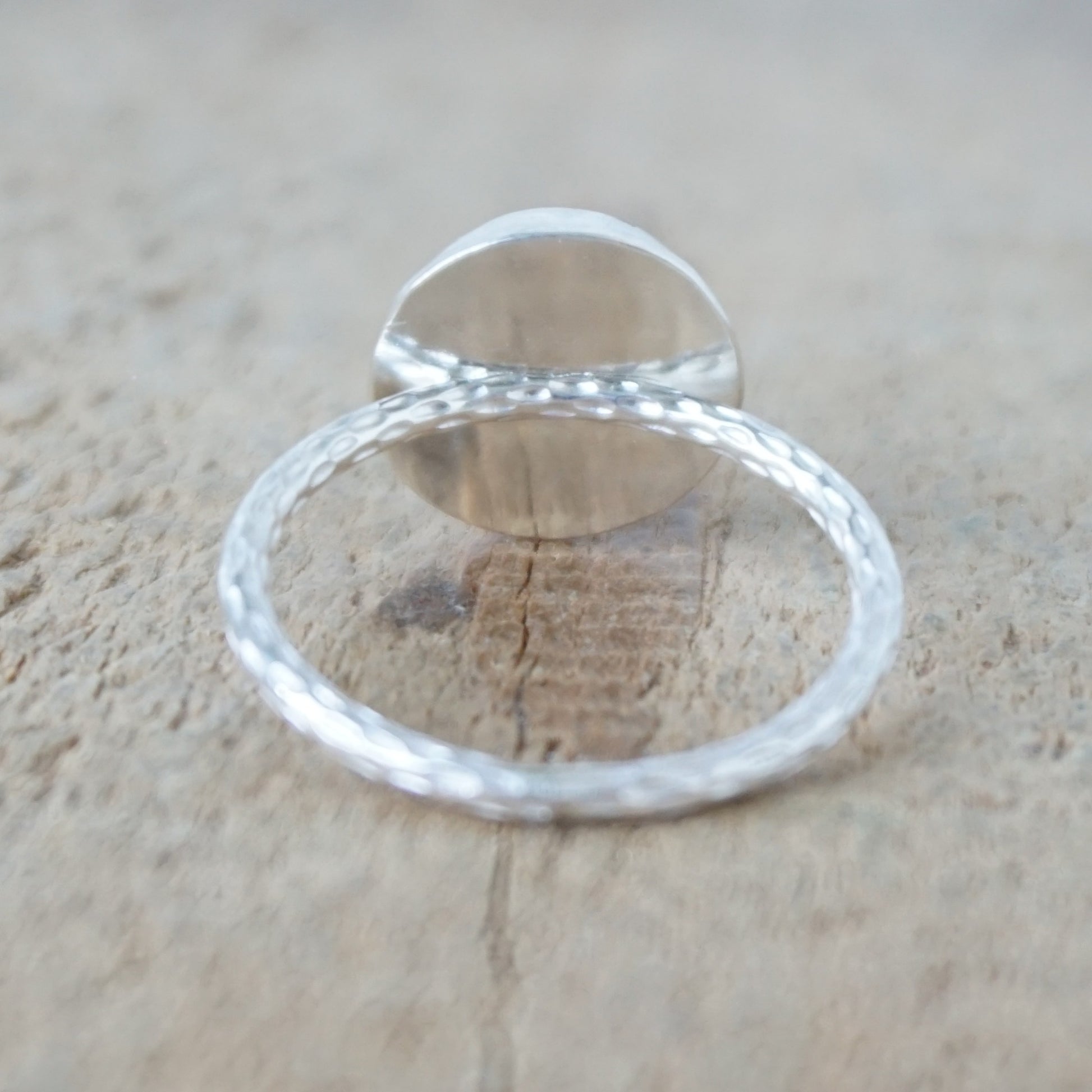 back view of A sterling silver ring featuring a round turquoise cabochon stone with natural dark veining, set against a neutral, textured beige background.